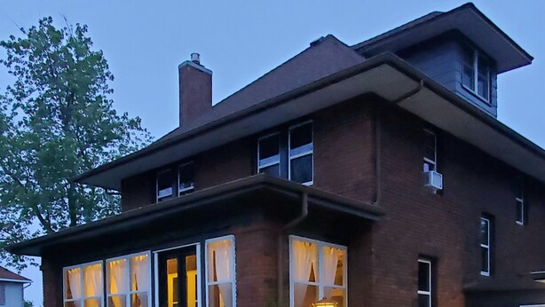 Une maison à deux étages, construite en briques, dotée de grandes fenêtres, d’un porche à l’avant et d’une pelouse bien entretenue.