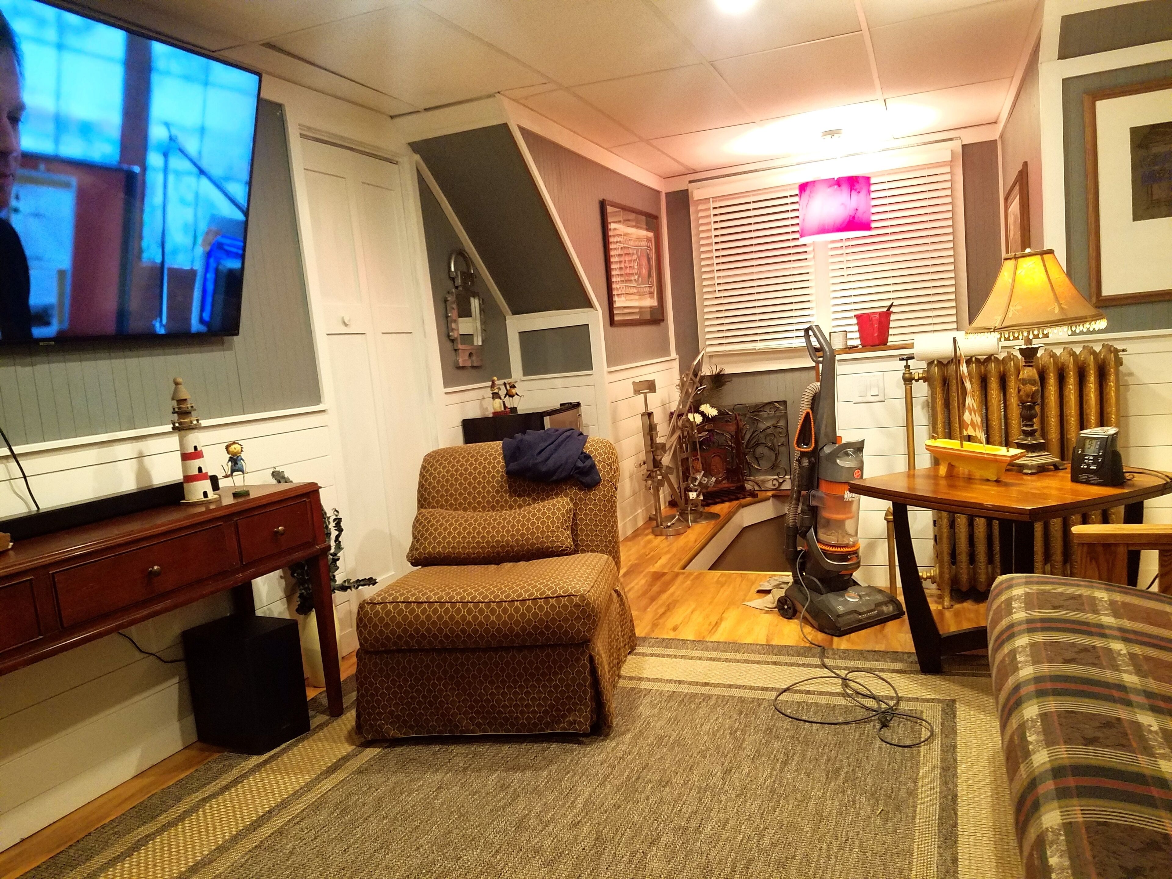 Una sala de estar acogedora con televisor, un sillón estampado, una mesita de noche con lámpara y un modelo decorativo de barco.