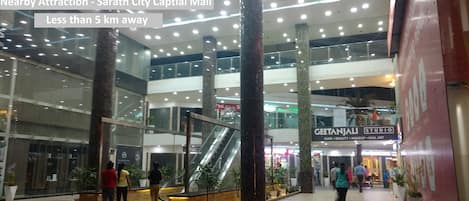 A multi-level shopping mall interior with escalators, glass railings, and potted plants.