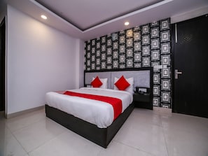 A modern hotel room with a large bed, white bedding, red accents, a patterned wallpaper, and a black door. - OYO 24943 Belmond Palace (New Delhi)