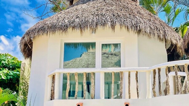 Un bâtiment à toit de chaume doté d’un balcon, entouré d’une végétation tropicale.