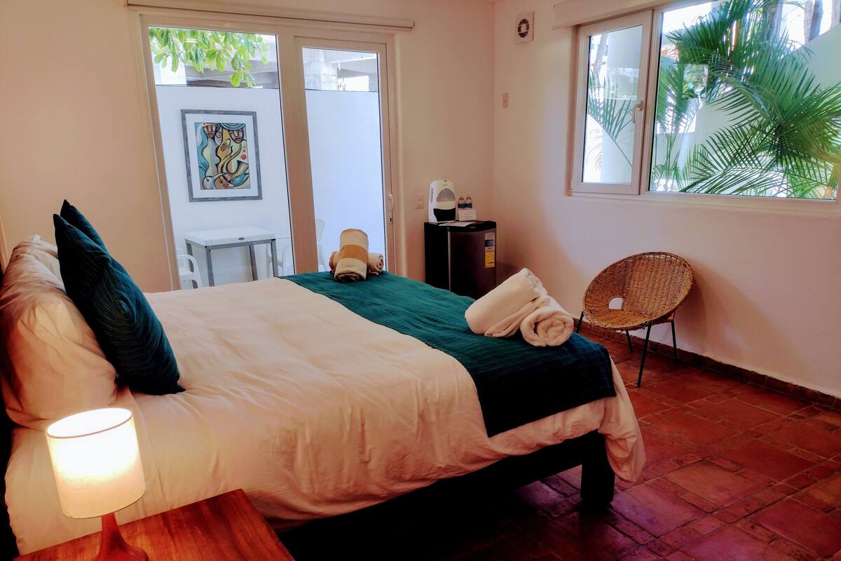 Un lit bien fait, avec une couverture verte, une lampe de chevet et une chaise.