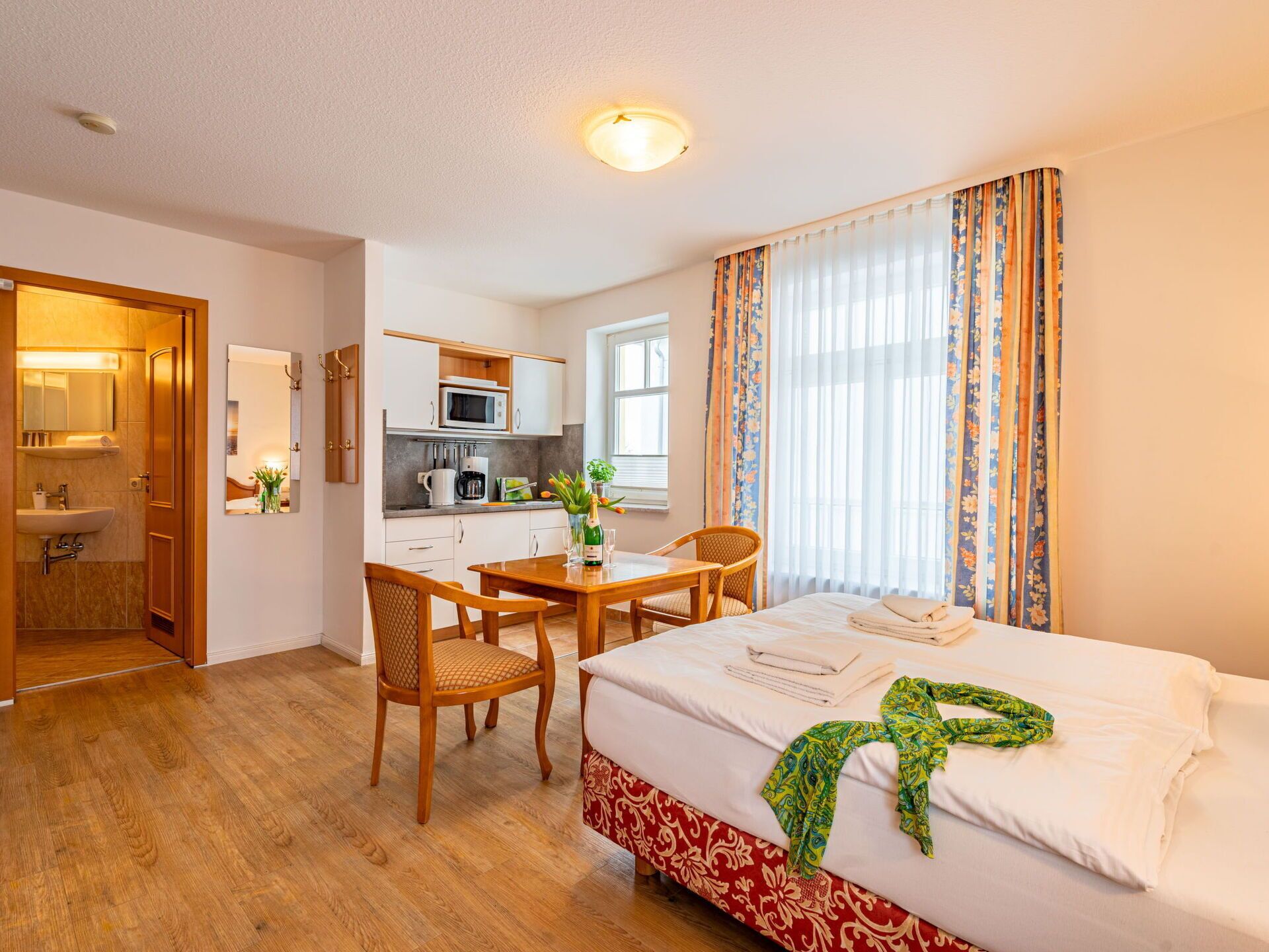 A hotel room with a bed, a dining table with chairs, a kitchen area, and a bathroom.