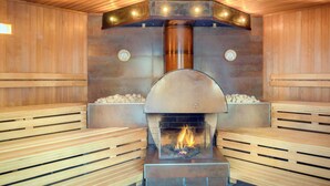 Un sauna avec des bancs en bois, un foyer central et un poêle en métal.