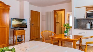 Une chambre d’hôtel comprenant un lit, une télévision, un bureau avec une chaise, une kitchenette et une salle de bain avec douche.