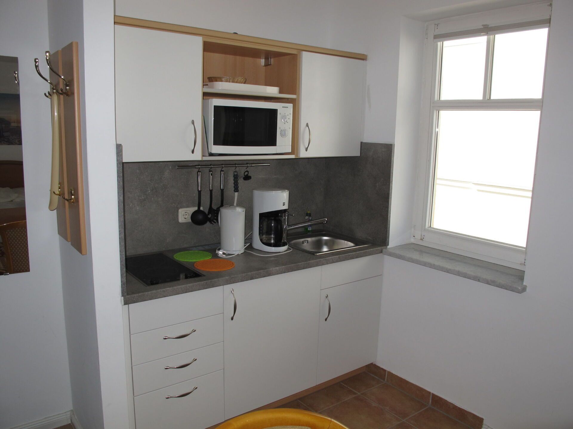 Una cocina compacta con muebles blancos, un microondas, una cafetera y un lavabo.