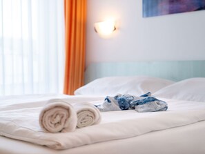 Een net opgemaakt bed met opgerolde handdoeken en een blauw geborduurd object op het bed.