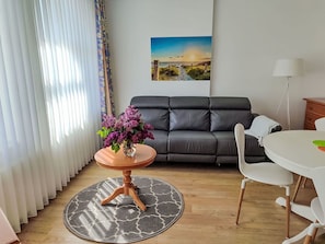 A living room with a sofa, a round table with chairs, a vase of flowers, and a painting on the wall.
