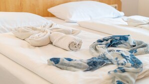 Siististi pedattu sänky, jossa on rullalle taitetut pyyhkeet ja sinikuvioinen peitto.