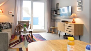 Ein modernes Wohnzimmer mit einer Couch, einem Esstisch mit einer Speisenplatte, einem Fernseher und einem Bücherregal.