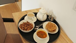 A tray with a cup of coffee, a bowl of cereal, a plate of flatbread, a bowl of soup, and a teapot on a wooden table. - OYO 847 Hotel Sinon (New Delhi)
