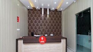 A reception desk with a patterned wallpaper backdrop, a modern ceiling design with recessed lighting, and a glass door entrance. - OYO 847 Hotel Sinon (New Delhi)
