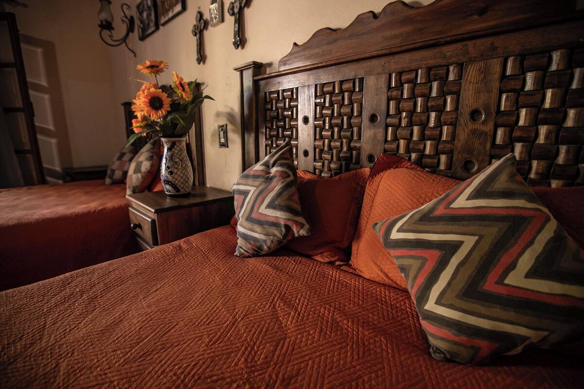 Een slaapkamer met een houten hoofdbord, een bed met een bedspreider met oranje textuur, en decoratieve kussens.