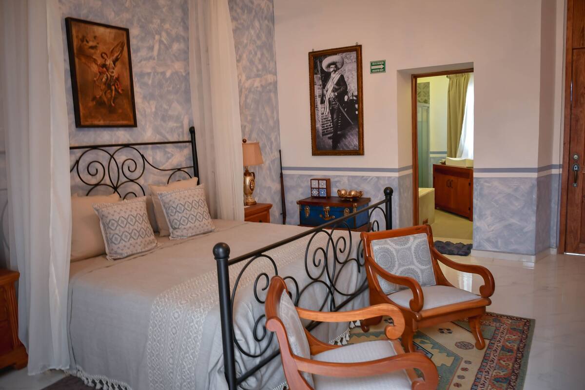 Een slaapkamer met een bed, twee stoelen, een nachtkastje en een dressoir.