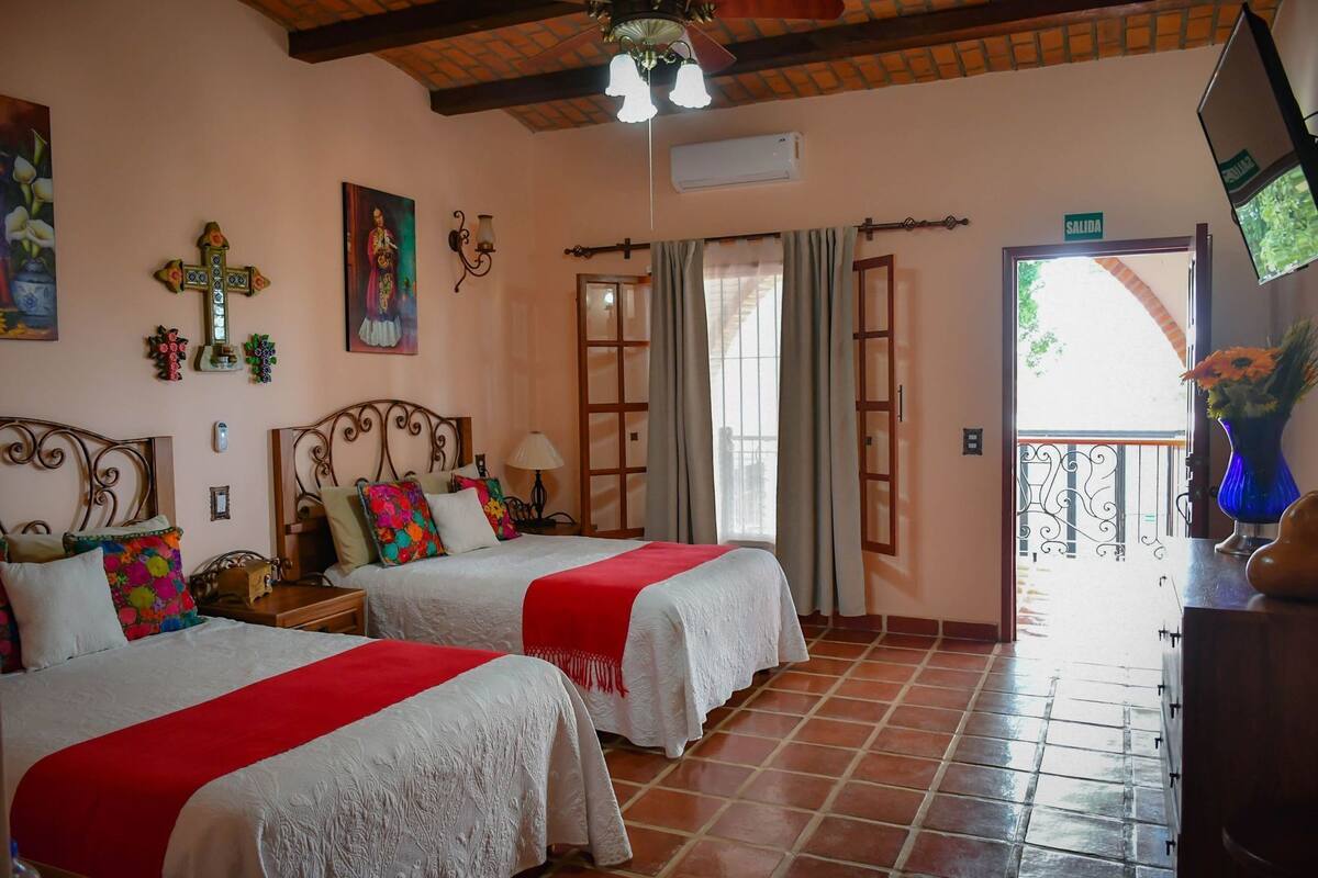 Een kamer met twee bedden, een televisie, een kruisdecoratie, een schilderij en een balkon met uitzicht.