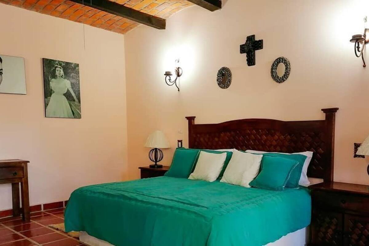 Een slaapkamer met een bed, twee nachtkastjes, een houten hoofdbord, decoratie aan de muur en een betegelde vloer.