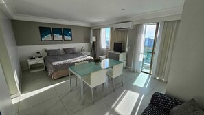 Camera d'albergo moderna con un letto, un tavolo da pranzo in vetro, una televisione e un balcone con tende.