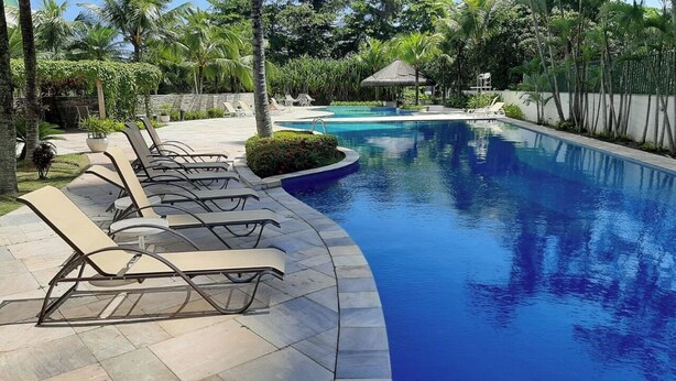 Une piscine avec des chaises longues et une structure surmontée d’un toit de chaume.