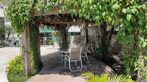 Un patio al aire libre con una mesa y sillas, rodeado de follaje y un muro de piedra.