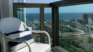 Une chaise blanche avec une bande bleue, placée sur un balcon d’où l’on peut admirer le paysage urbain et la vue sur l’océan.