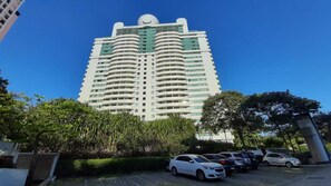 Un edificio alto y moderno con fachada curva, rodeado de coches aparcados y vegetación.
