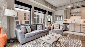 Ein modernes Wohnzimmer mit einem grauen Sofa, einem gemusterten Teppich und einem Couchtisch mit einem Buch und einer Fernbedienung.