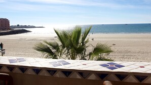 A beach view with a tiled balcony, palm trees, and a distant shoreline.