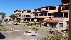 A multi-story hotel with a courtyard featuring a swimming pool, palm trees, and outdoor seating areas.