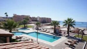 A resort with a swimming pool, lounge chairs, and a view of the beach.