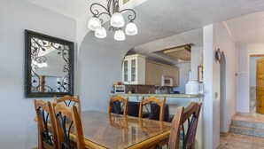 Un coin repas avec une table et des chaises en bois, un lustre et une cuisine en arrière-plan.