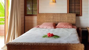A bedroom with a bed, two windows with blinds, a wall-mounted light fixture, and a view of greenery outside. - Villa Tea by Tahiti Homes (Moorea-Maiao)