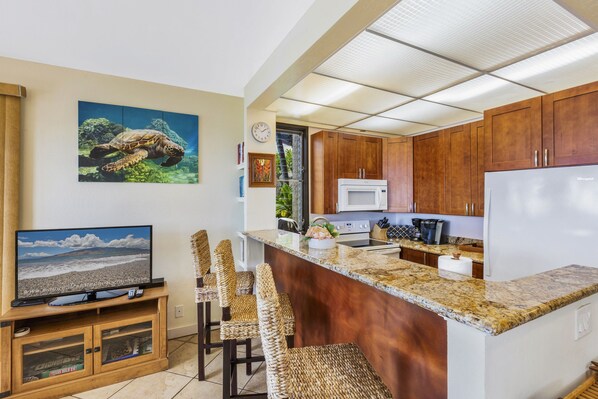 Una cocina moderna con armarios de madera, encimera de granito, microondas integrado y una isla grande con taburetes de bar.