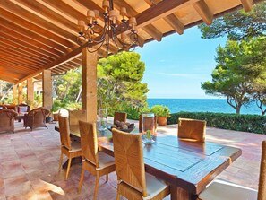 Une terrasse extérieure aménagée avec des meubles en osier, une table en bois et une vue sur la mer.
