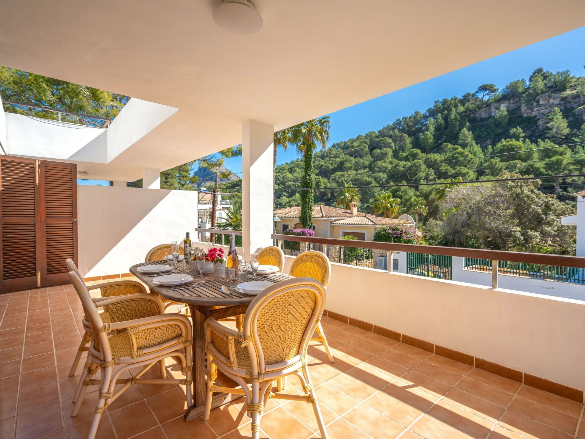 A terrace with a table set for dining, wicker chairs, and a view of a mountainous landscape.