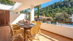 Une terrasse avec une table dressée pour le repas, des chaises en osier et une vue sur un paysage montagneux.