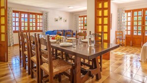 Un coin repas avec une table et des chaises en bois, un canapé bleu et de grandes fenêtres à cadre en bois.