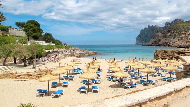 Une plage avec des chaises longues et des parasols, une côte rocheuse et un ciel dégagé.