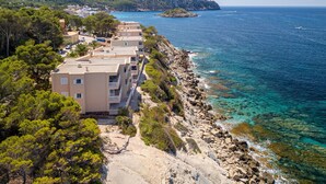 Un hotel costero con varias edificaciones a lo largo de la orilla, mar azul cristalino y un paisaje montañoso al fondo.