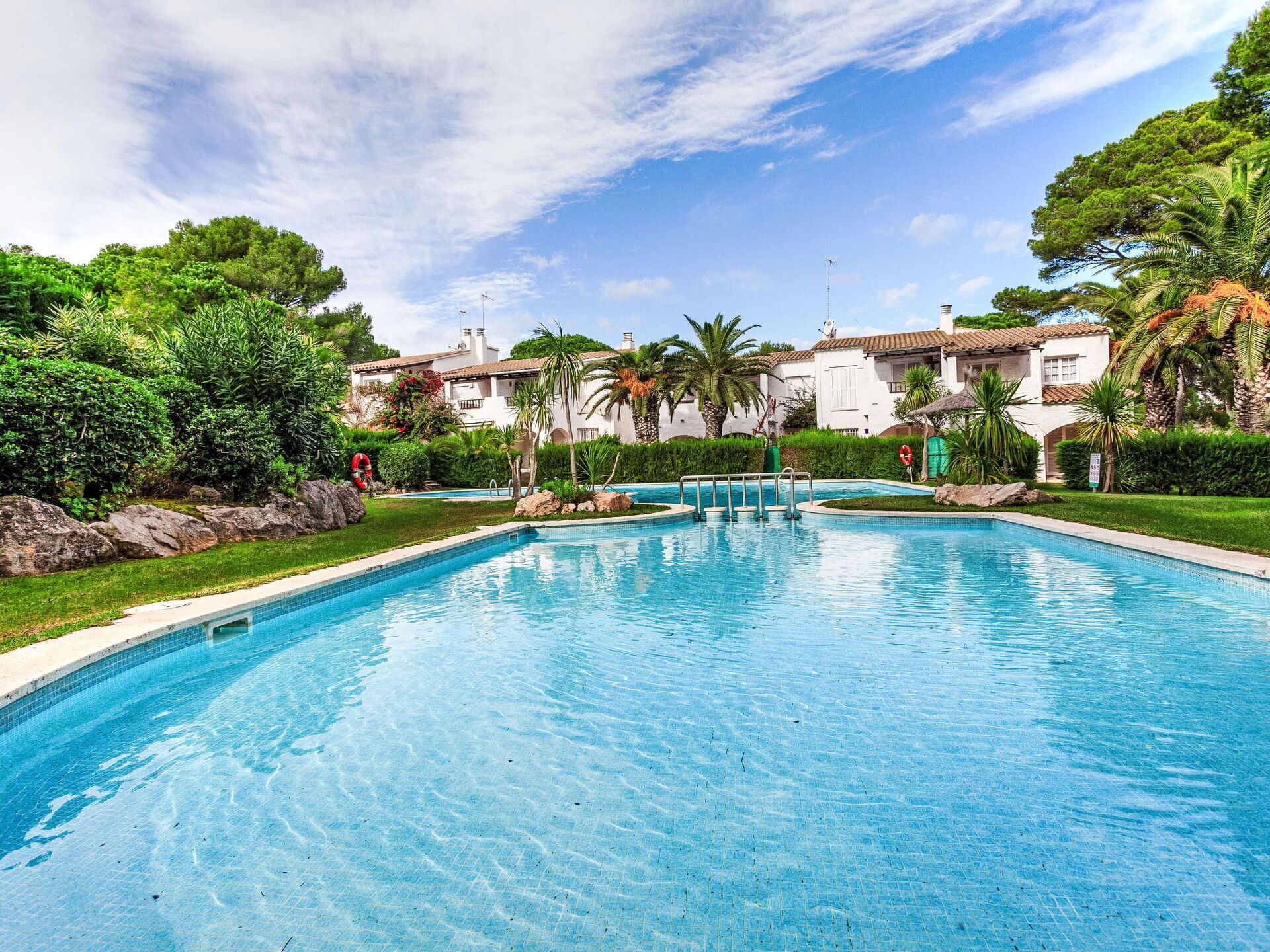 A swimming pool surrounded by lush greenery and white buildings with red-tiled roofs.