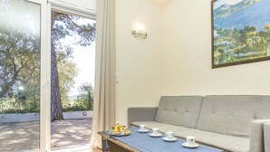 Une pièce avec un canapé, une table sur laquelle sont disposés des tasses et des pâtisseries, un tableau au mur et une vue à travers une porte vitrée.