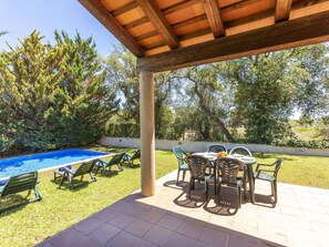 Un patio techado con piscina, mobiliario exterior y vista a árboles.