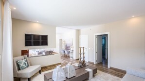 Una sala de estar moderna con sofá, una mesa de centro y elementos decorativos. Se observa un comedor con sillas y una mesa al fondo.