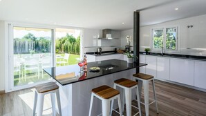 Una cocina moderna con una isla central, armarios blancos y vistas a un jardín a través de amplios ventanales.