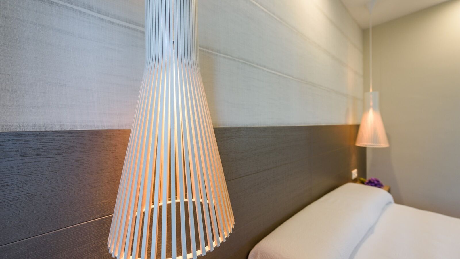 A hotel room with a bed, a hanging lamp, and a wall with a wood panel design.