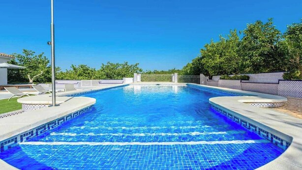 Una piscina rectangular con borde de azulejos, rodeada por un muro bajo y una valla.