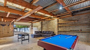 Une table de billard dans une pièce aux poutres apparentes et aux murs en briques.