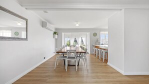 A spacious dining area with a wooden table and white chairs, a kitchen with bar stools, and a large mirror on the wall.