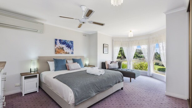 A modern bedroom with a large bed, bedside tables, a ceiling fan, and a window with curtains.
