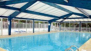 An indoor swimming pool with clear blue water, surrounded by white lounge chairs and a covered roof structure. - Lovely apartment in villa for 4 guests with WIFI, pool, TV, terrace and pets allowed (Saint-hilaire-de-riez)