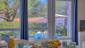Aamiaispöytä, jossa on croissantteja, hedelmiä ja kahvikuppeja, ja taustalla ikkuna, josta avautuu näkymä puihin ja rakennuksiin.